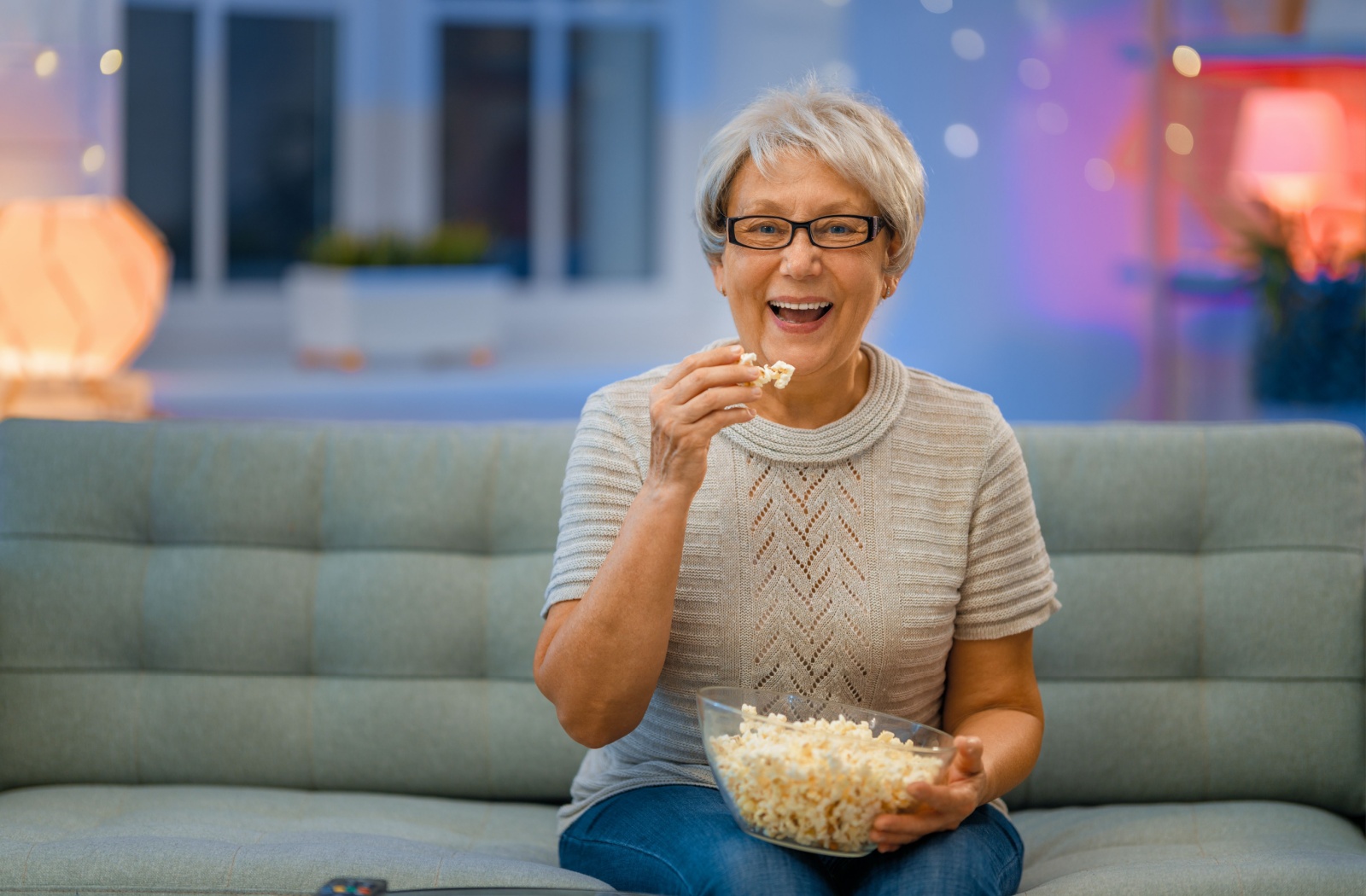 An older adult sitting on their couch with a bowl of popcorn, preparing to watch a movie.