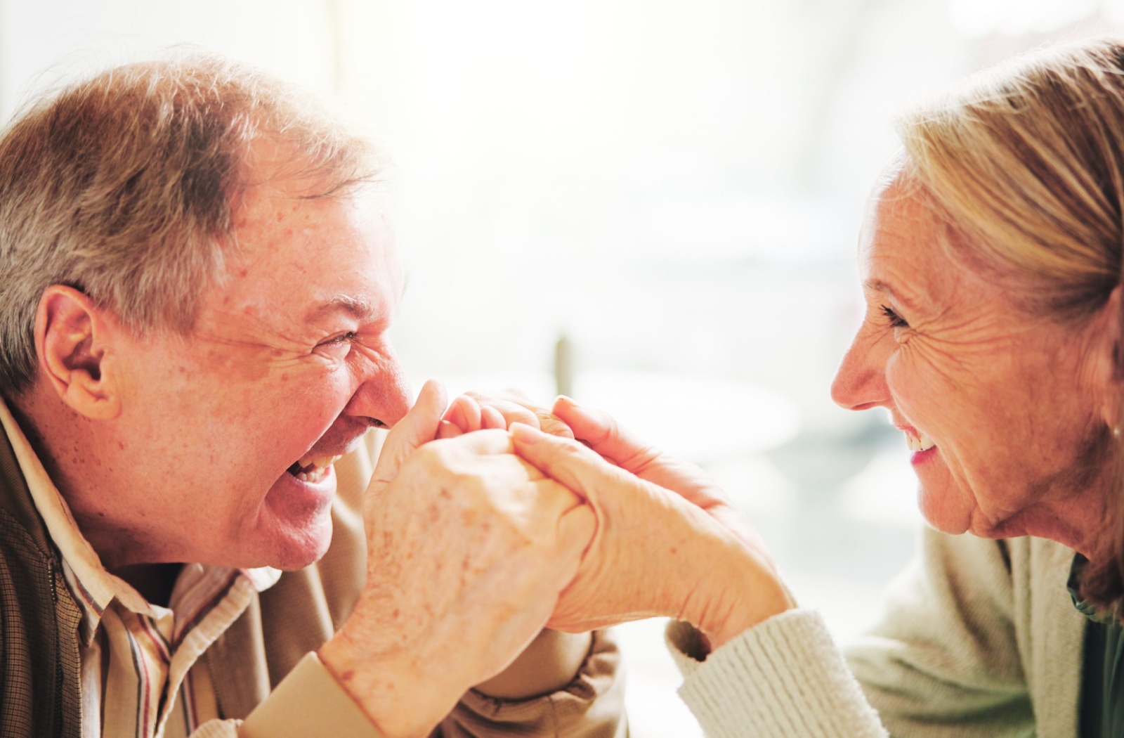 Senior couple laughing and holding hands during a joyful moment in a memory care setting