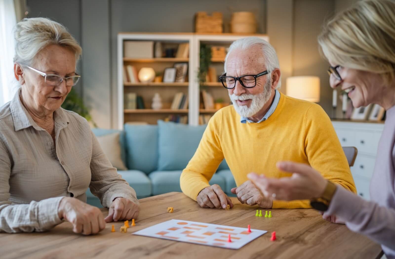 3 older adults play a tabletop game and laugh together in an apartment in senior living
