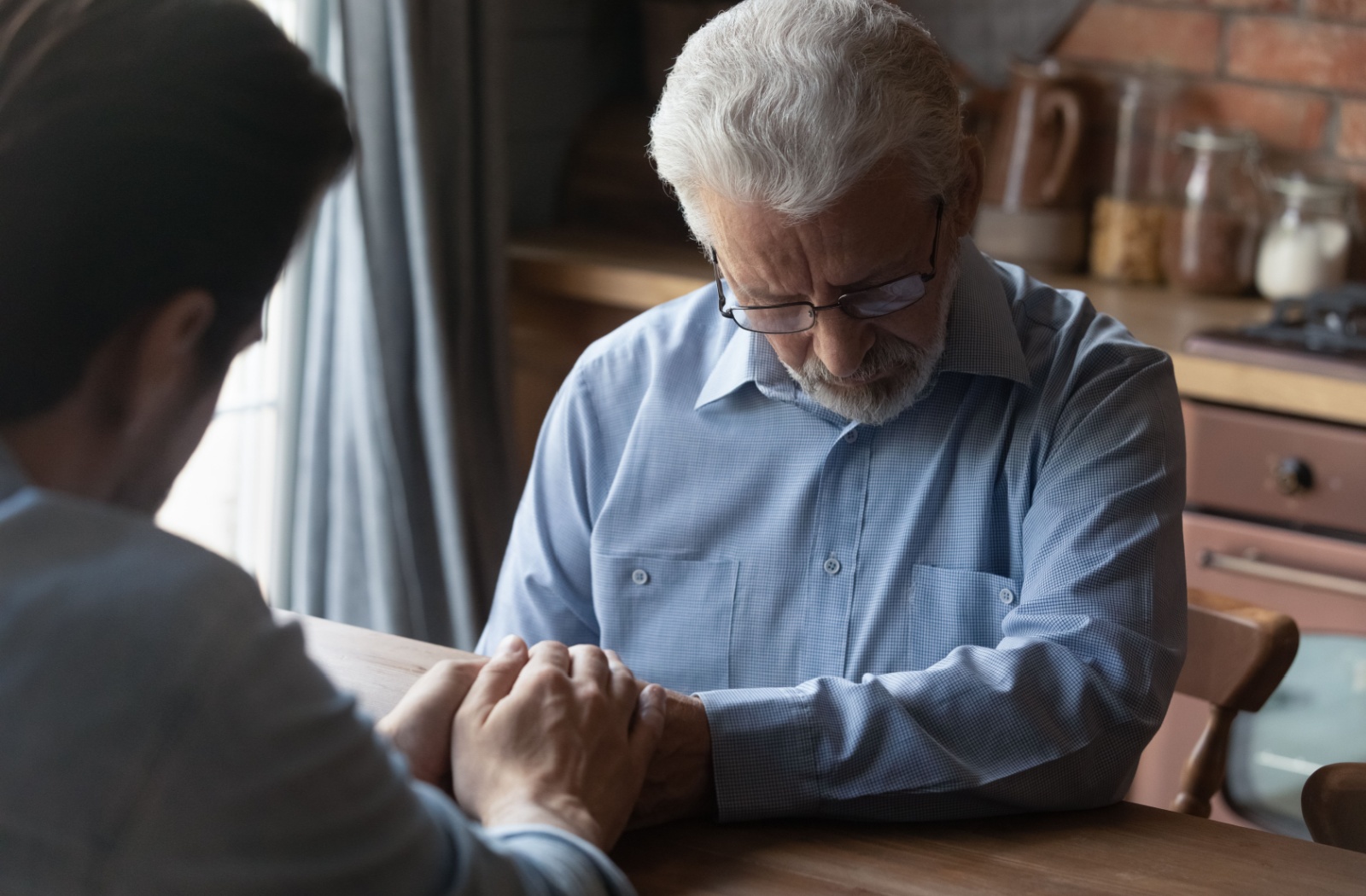 An adult child grasps the hands of their senior parent who is living with dementia.
